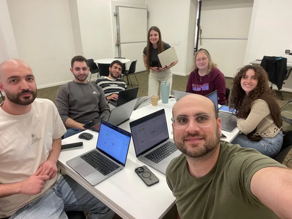 A group gathered around a table with open laptops.